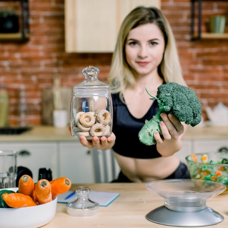 young-woman-in-black-sport-clothes-choosing-between-broccoli-or-junk-food-bagels-healthy-clean-1.jpg
